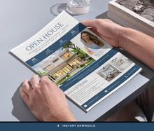 A person holds an open real estate open house brochure over a gray tabletop. The brochure has a white and navy design with property photos, text, and a woman's portrait.