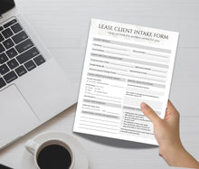 A hand holding a printed 'Lease Client Intake Form' over a desk with a laptop, coffee cup, and notepad.